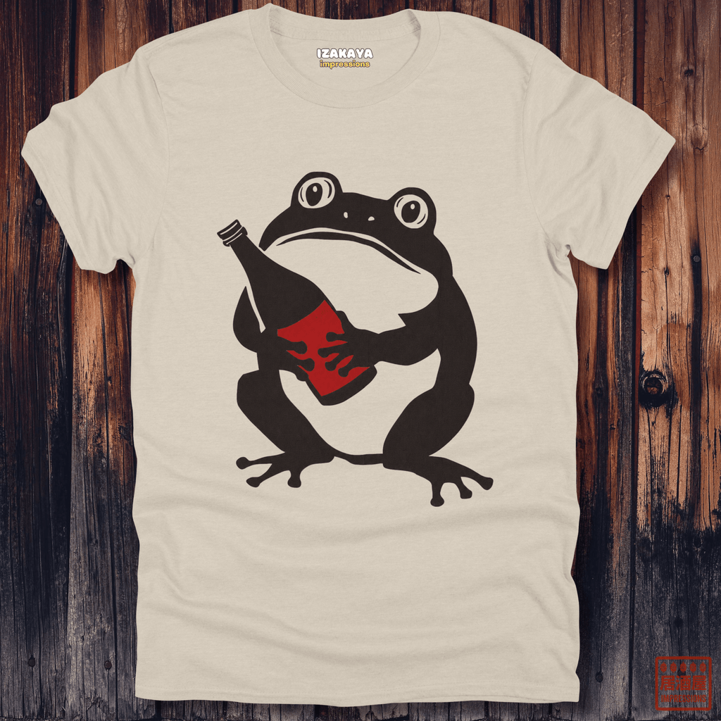 An off-white t-shirt with a graphic of a black frog holding a red bottle, displayed flat on a dark wood background. The brand name 'IZAKAYA' is visible on the inner neck label.